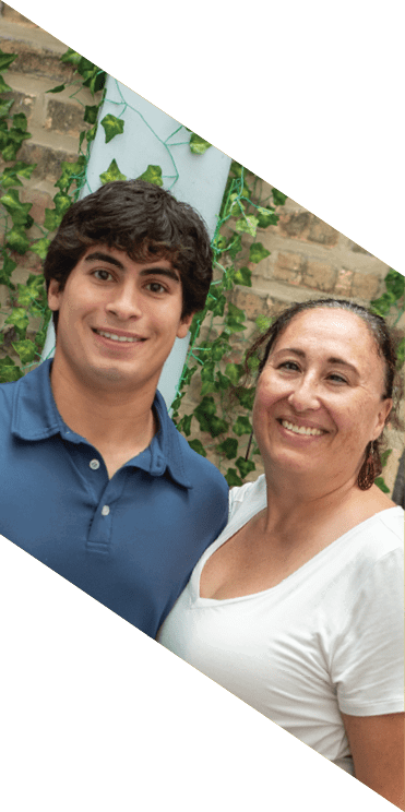 A person with short curly hair wearing a blue collared shirt is smiling in front of a leafy background. Description generated by AI