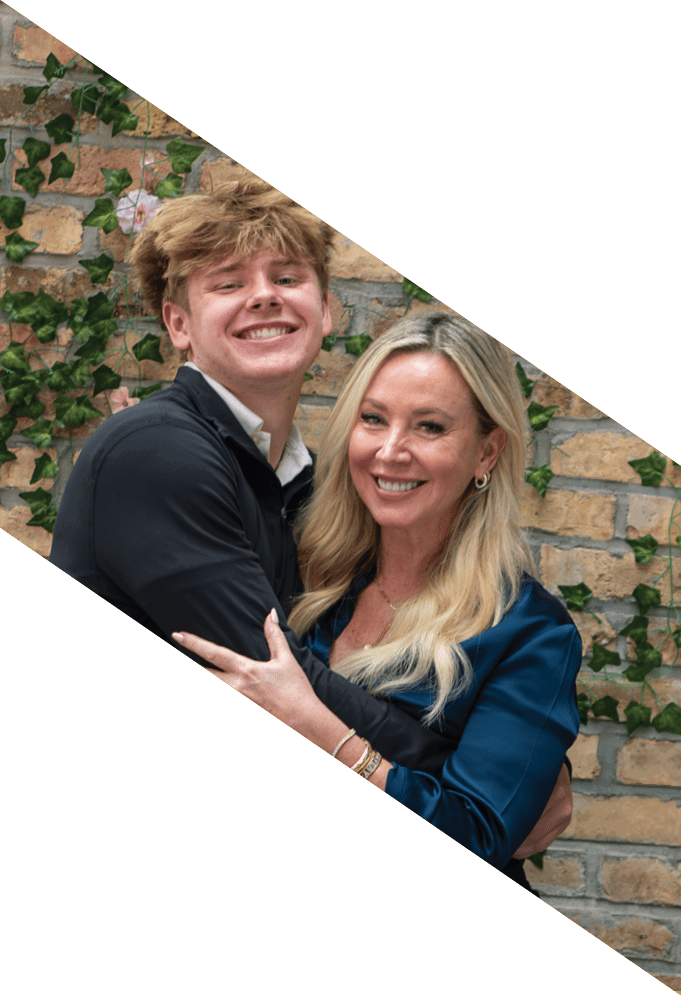 Two people with light-colored hair are smiling and posing closely together in front of a brick wall with green ivy. Description generated by AI