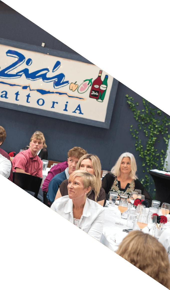 A group of people seated around a long table in a restaurant setting, attentively listening to something or someone. Description generated by AI