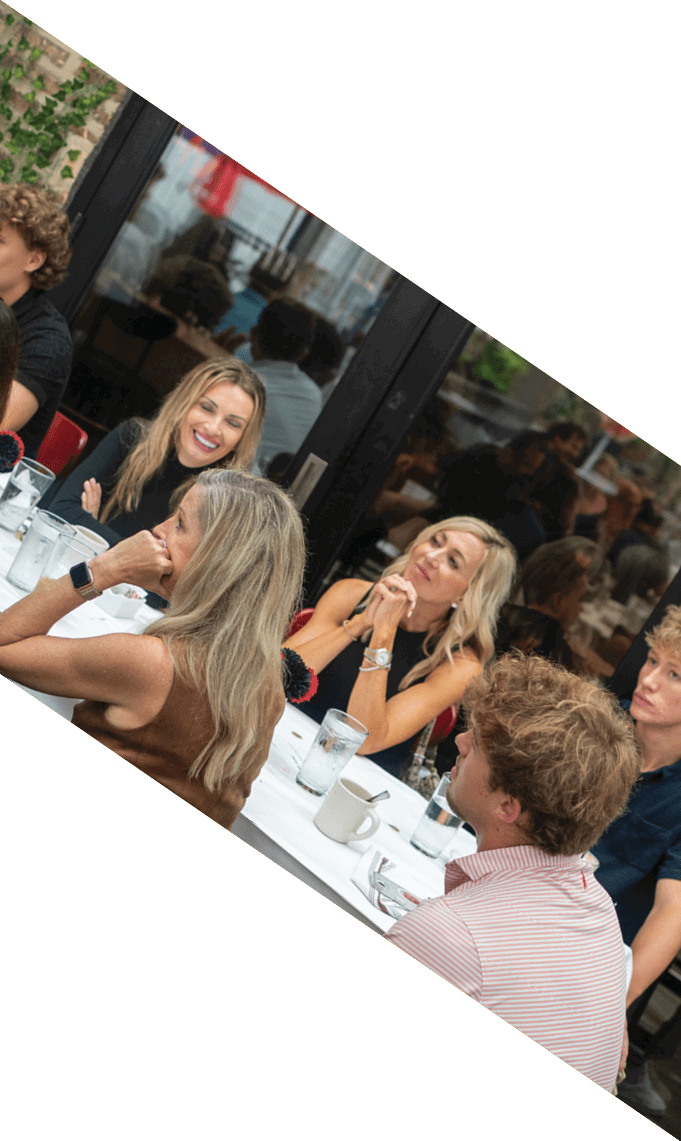 Several adults with varied hairstyles are seated around a table with drinks and a pitcher, engaged in conversation in a casual indoor setting. Description generated by AI