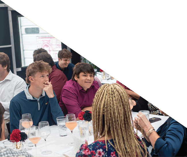 Adults sitting at a table in a casual dining setting with a chalkboard menu and plants in the background. Description generated by AI