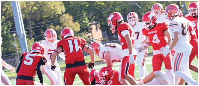 People wearing red and white football uniforms are engaged in a play on a green field with one person on the ground and others standing or crouching around. Description generated by AI