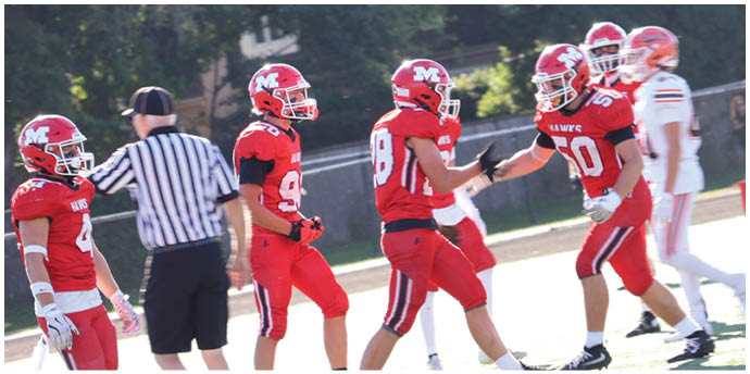Adults in red football uniforms are celebrating on a sunlit field while an official and players in white uniforms stand nearby. Description generated by AI