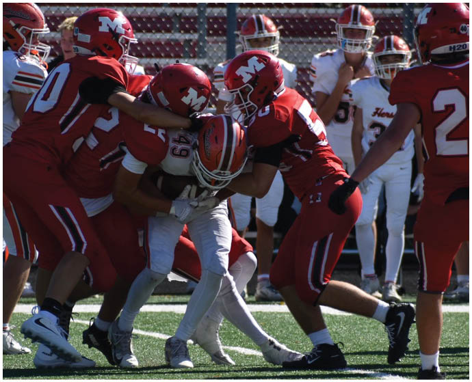Several football players in red uniforms are tackling a player in a white uniform on a grassy field during a game. Description generated by AI