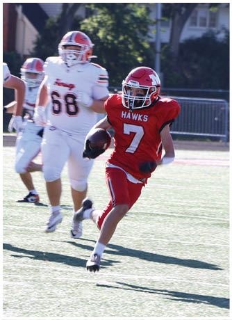 Three people in white football uniforms are running on a field while one person in a red uniform is holding a football and running away from them. Description generated by AI