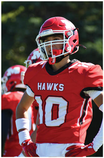 People wearing red football uniforms and helmets are standing outdoors, with one person prominently in the foreground wearing a white wristband and gloves. Description generated by AI
