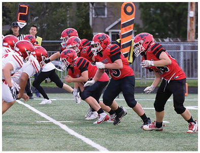 Players in red and white football uniforms are lined up facing each other on a field, preparing for the next play. Description generated by AI