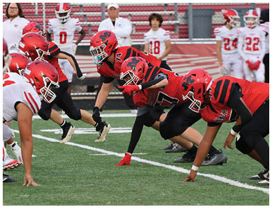 Two opposing football teams in red and white uniforms are lined up facing each other on a field, ready for the next play. Description generated by AI