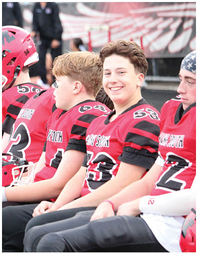 Several people wearing red sports jerseys are sitting together, with one person holding a red helmet and another wearing a red helmet. Description generated by AI