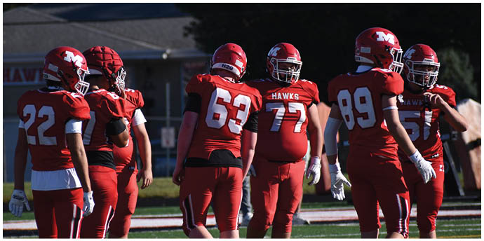 A group of people wearing red football uniforms and helmets are standing together on a football field during daylight. Description generated by AI