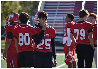 Two people wearing red football jerseys with numbers 25 and 80 stand on a field, with one person holding their hand near their face. Description generated by AI