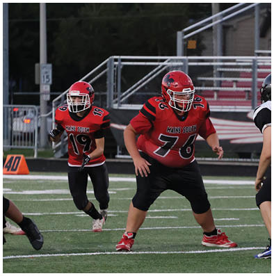Children in football uniforms are positioned on a field preparing for a play during a game. Description generated by AI