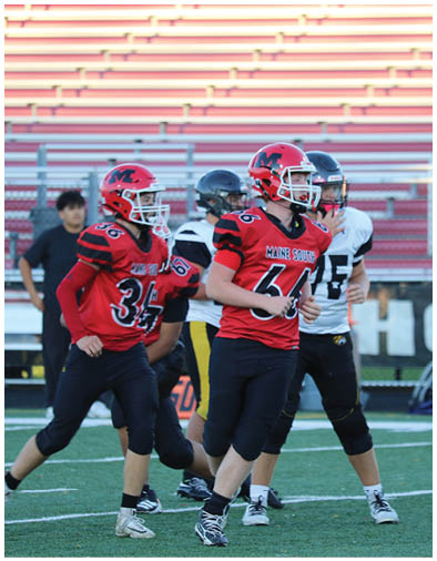 People wearing football uniforms are on a field with bleachers in the background, appearing to be engaged in a game or practice. Description generated by AI