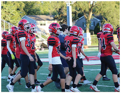 A group of people wearing red and black football uniforms and helmets are walking together on a football field. Description generated by AI