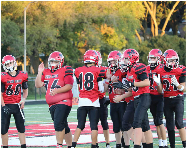 A group of people wearing red and black football uniforms are standing together on a field with trees in the background. Description generated by AI