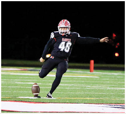 A person wearing a football helmet and uniform is extending one arm forward against a dark background. Description generated by AI