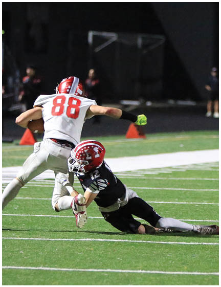 Two people in football uniforms are engaged in a play on a well-lit field during a nighttime game. Description generated by AI