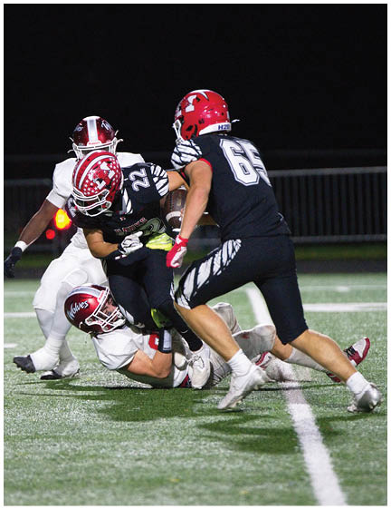 A group of people wearing football uniforms are engaged in a tackle on a lit field during a nighttime game. Description generated by AI