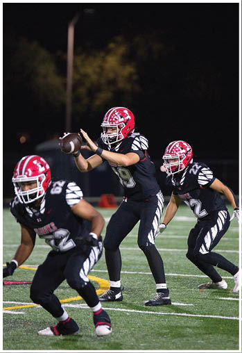 Two people in black and white football uniforms with red helmets are positioned on a football field during a game. Description generated by AI