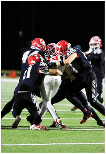 Two people in football uniforms are engaged in a tackle on a grassy field during a game. Description generated by AI