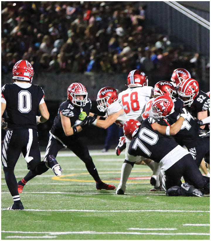 People wearing football uniforms with red helmets are engaged in a tackle during a game on a grassy field. Description generated by AI