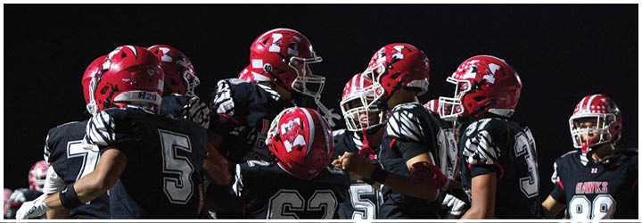 A group of people wearing red helmets and black sports uniforms are gathered closely together, likely participating in a football game. Description generated by AI