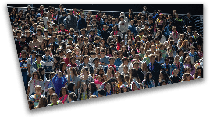 A large crowd of people wearing casual clothing is gathered closely together, some appearing to be cheering or engaged in an event. Description generated by AI