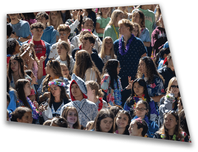 A large group of people wearing colorful and casual clothing are gathered closely together, some smiling and interacting in an outdoor setting. Description generated by AI