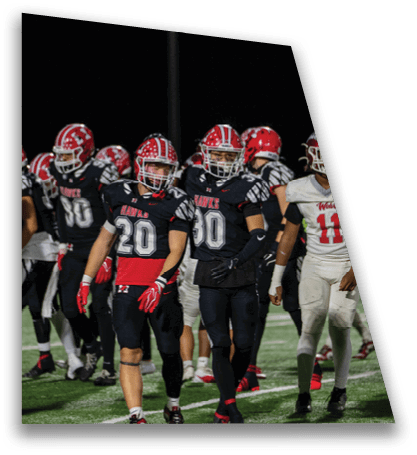 Adults wearing football uniforms and helmets are gathered on a field under stadium lights during a nighttime game. Description generated by AI