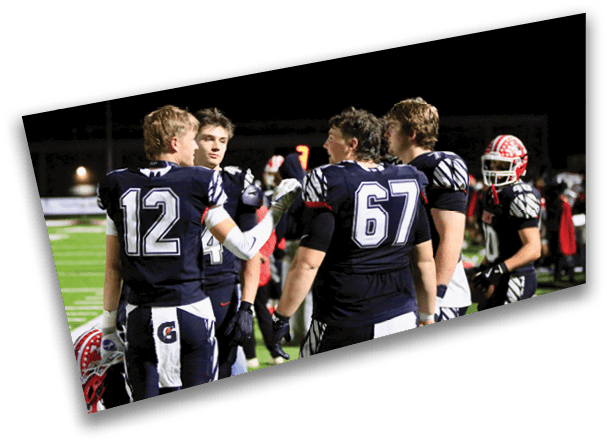 Four people in dark football uniforms with numbers 12, 40, 67, and 7 are standing together on a field at night. Description generated by AI