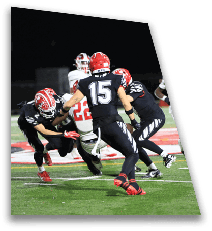 People wearing football uniforms are actively engaged in a play on a well-lit field at night. Description generated by AI