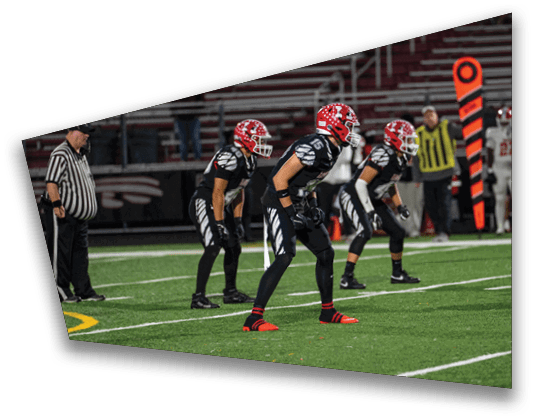 Several people in football uniforms are positioned on a field, appearing ready for a play during a game. Description generated by AI
