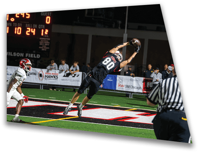 A person in a black football uniform is leaping to catch a football near the end zone while another person in a white uniform and a referee watch. Description generated by AI
