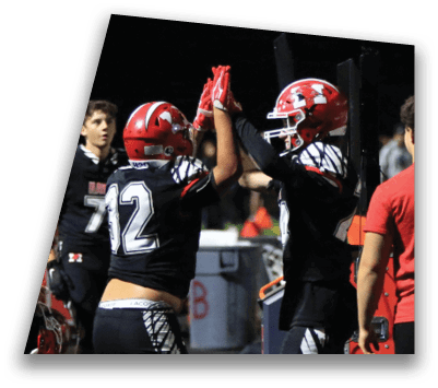 Two people wearing black football uniforms and red helmets are giving each other a high five on a field at night. Description generated by AI