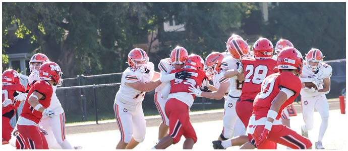 People wearing red and white football uniforms are actively engaged in a game on a grassy field. Description generated by AI