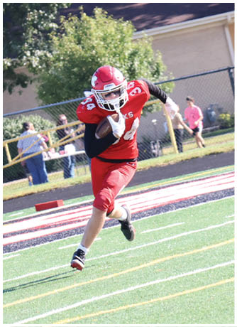 A person wearing a red football uniform and helmet is running on a green field holding a football. Description generated by AI