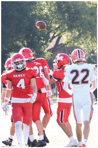 Several people wearing red and white football uniforms are on a field with one person in white preparing to catch a football in midair. Description generated by AI