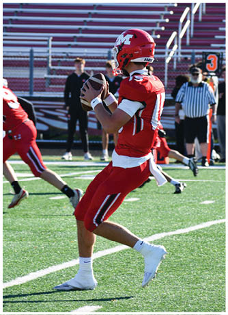 A person wearing a red football helmet and jersey stands on a field with empty bleachers and a few people in the background near a down marker showing the number three. Description generated by AI