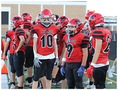 A group of people wearing red and black football uniforms and helmets are standing together on a field. Description generated by AI