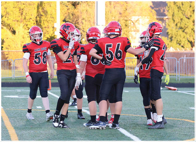 A group of six people wearing red and black football uniforms and helmets are standing together on a football field during daylight. Description generated by AI