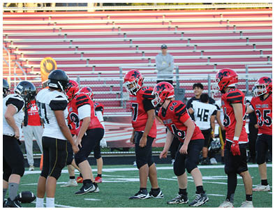 People in football uniforms from two teams are lined up facing each other on a field with empty bleachers in the background. Description generated by AI