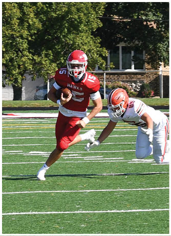 A person in a red sports uniform is running with a football on a green field while several people in white uniforms chase behind. Description generated by AI