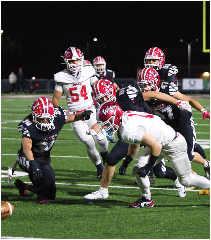Players in football uniforms are actively engaged in a play on a well-lit field at night, with some players in white and others in black jerseys. Description generated by AI