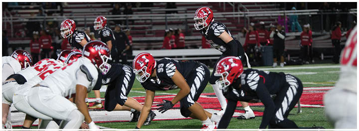 Two opposing American football teams in black and white uniforms are lined up on the field facing each other, ready for the next play. Description generated by AI