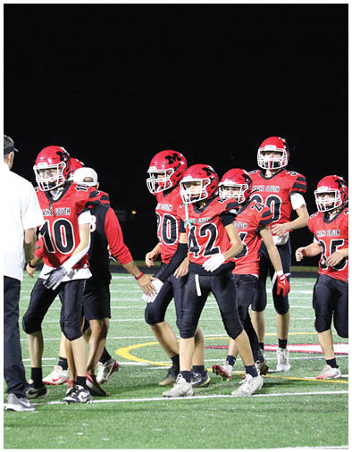 A group of people wearing red and black football uniforms and helmets are standing together on a football field at night. Description generated by AI