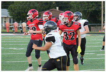 Several people wearing football uniforms are on a field with one person in a red jersey standing near others in white and black jerseys during a game or practice. Description generated by AI