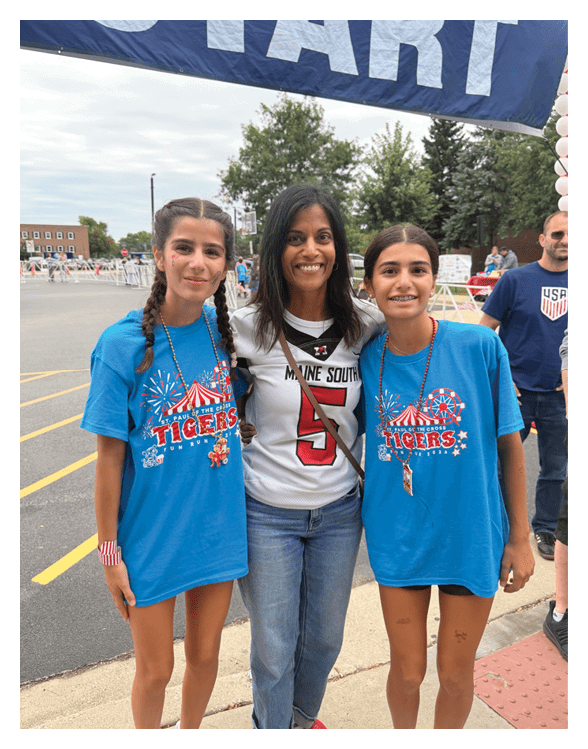 Three smiling people with braided and straight hair stand close together outdoors under a large banner with trees and a basketball hoop in the background. Description generated by AI