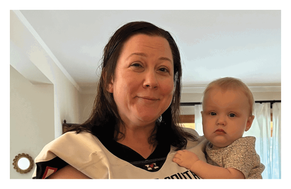 An adult with wet hair is holding a newborn wrapped in a white blanket in a softly lit indoor setting. Description generated by AI