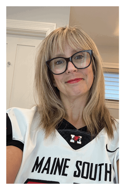 A person with straight blonde hair and bangs is wearing large black-framed glasses and red lipstick while smiling slightly. Description generated by AI