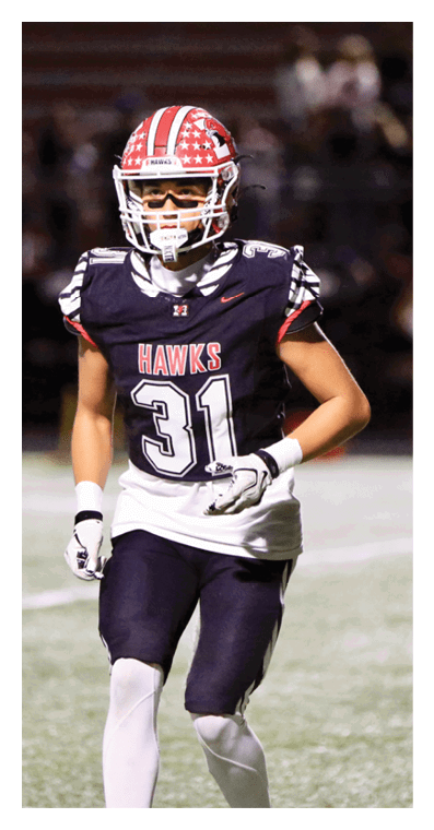 A person wearing a black football uniform with the number 31 and the word “HAWKS" on the jersey is running on a field. Description generated by AI